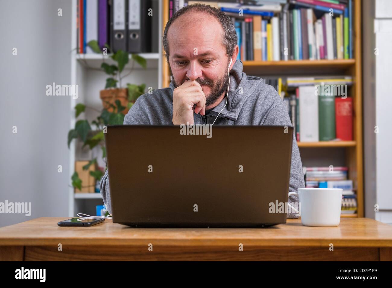 Homme travaillant en ligne depuis un bureau à domicile sur un ordinateur portable derrière un bureau d'époque, concentré, avec des écouteurs, à l'écoute de la réunion en ligne Banque D'Images