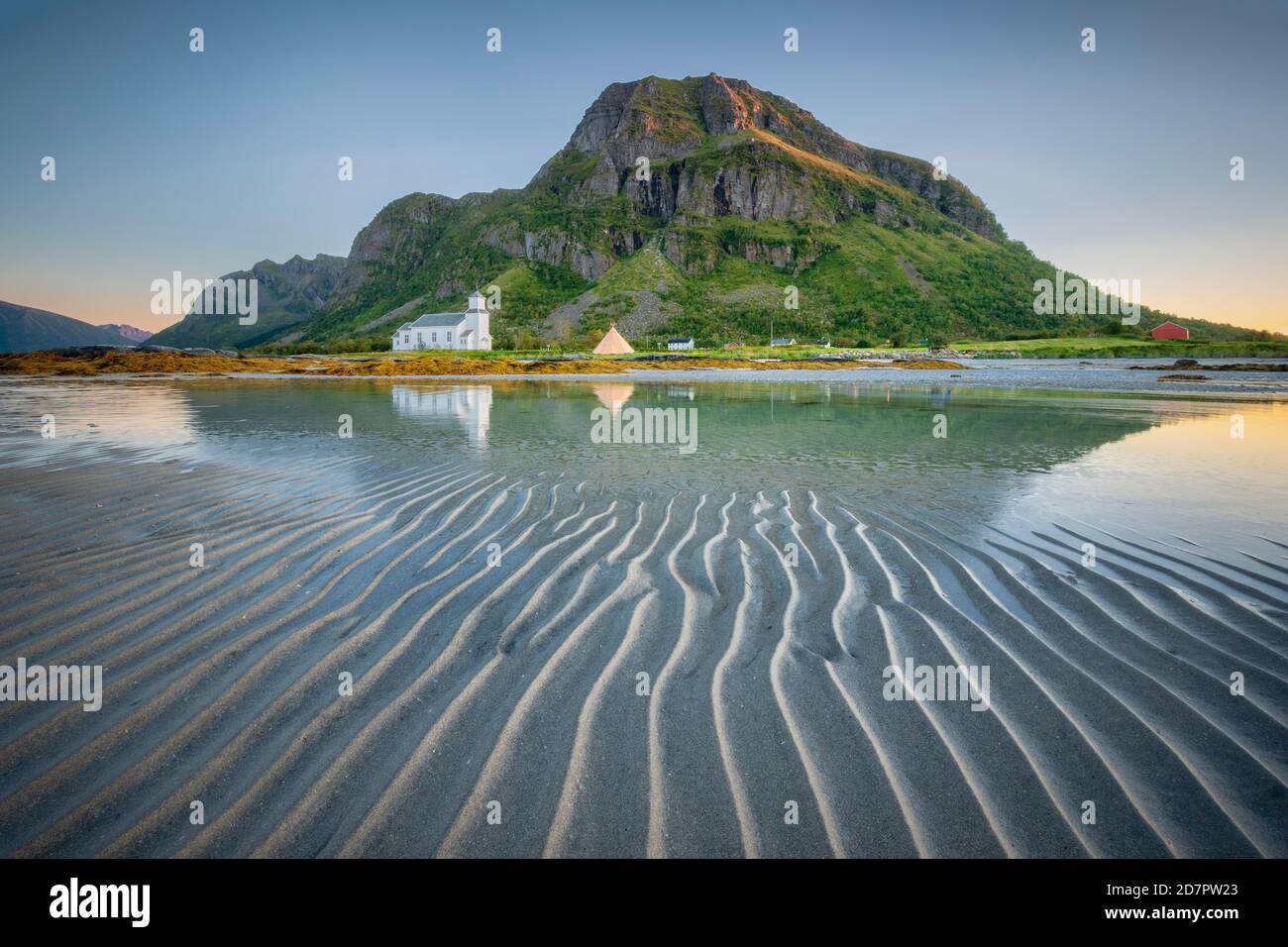 L'église de Gimsoy se reflète dans la mer à marée basse, en face plage de sable avec structure striée, derrière la montagne en soirée soleil, végétation verte sur Banque D'Images
