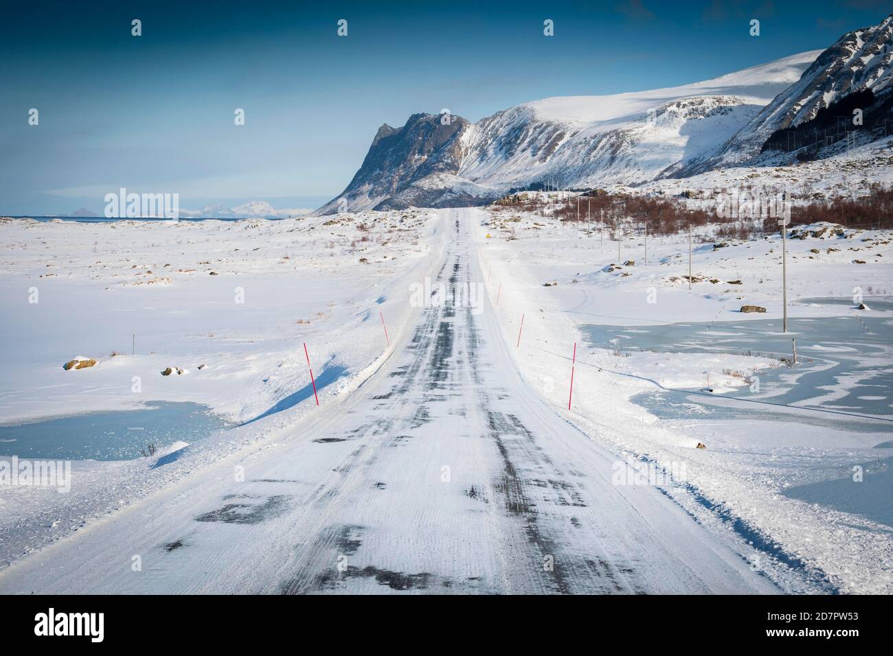 Route enneigée glacée, en paysage d'hiver, derrière la chaîne de montagnes et la mer, Nordland, Lofoten, Norvège Banque D'Images