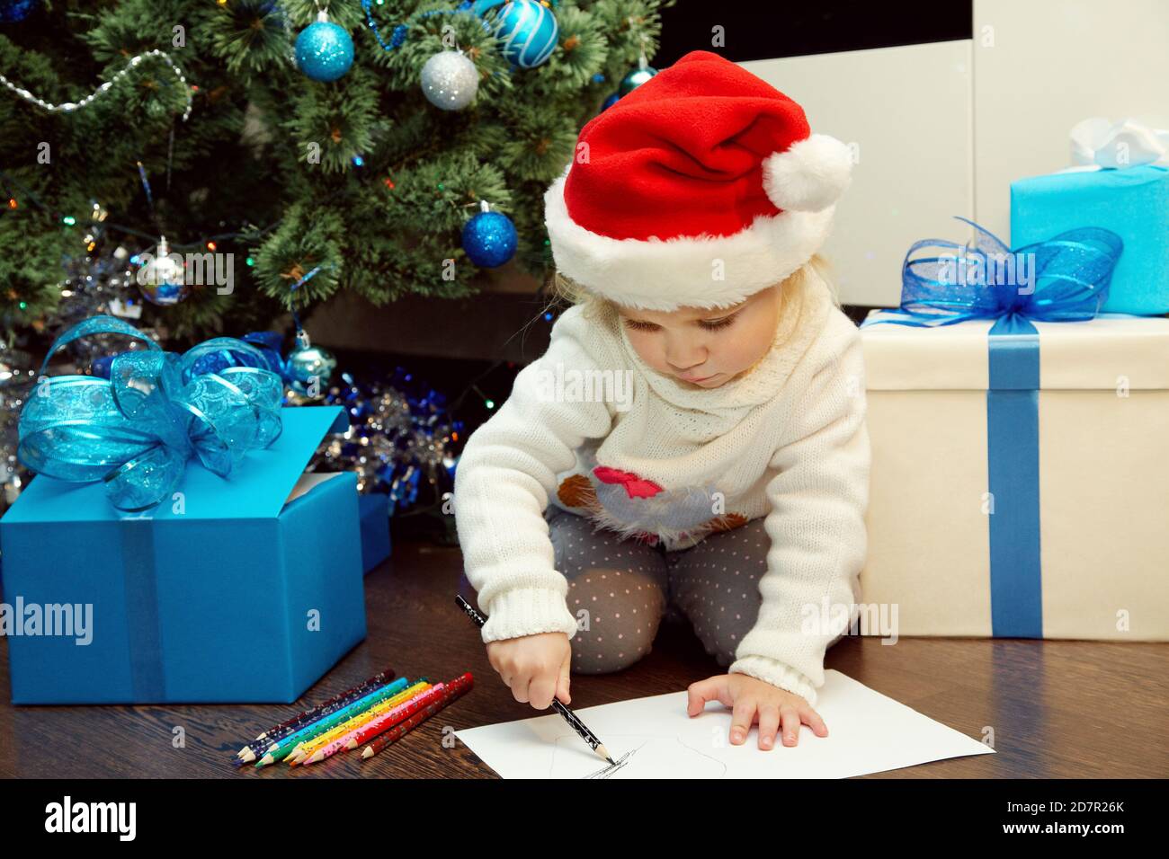 Jolie petite fille dans chapeau de père noël écrire une lettre à Le Père Noël près de l'arbre de Noël Banque D'Images