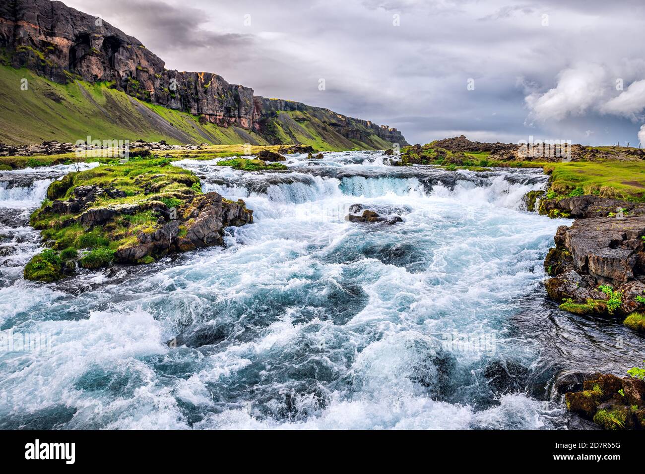 Vue sur le paysage de la rivière Rushing par le canyon Fjadrargljufur en Islande avec raides ruisseau d'eau par la mousse d'herbe verte et ciel nuageux Banque D'Images