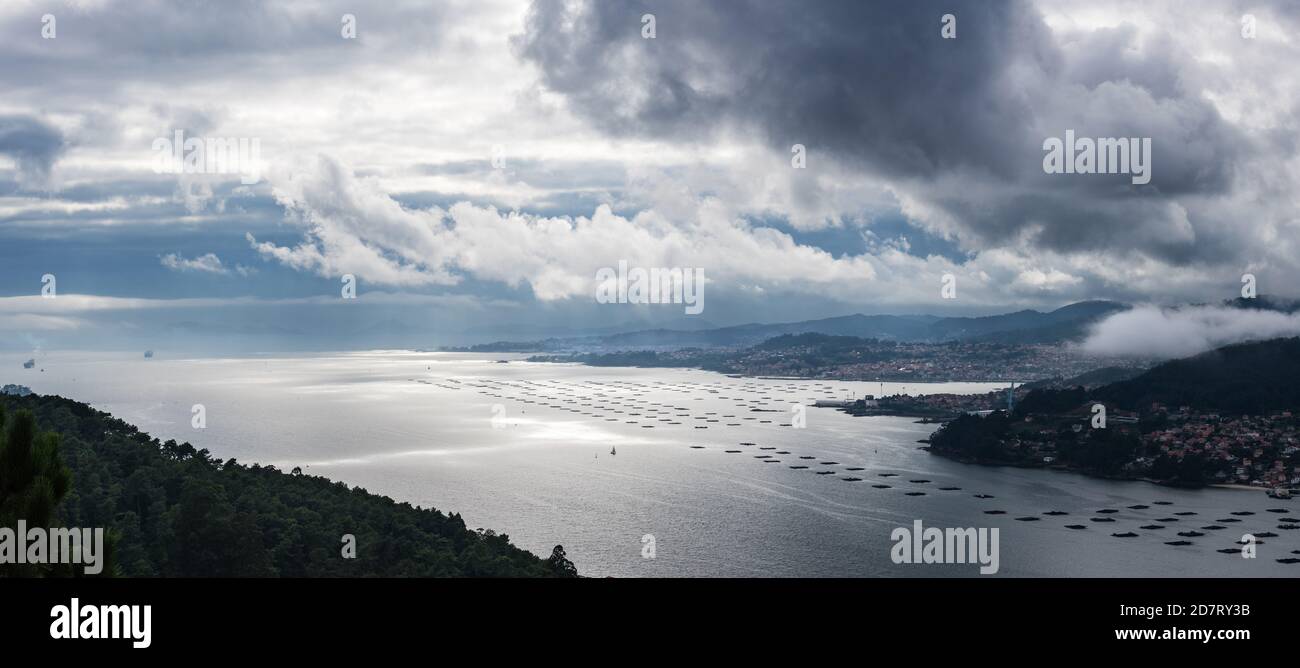 Vue panoramique de l'estuaire de la Ria de Vigo depuis Redondela, un après-midi d'été nuageux, avec l'océan Atlantique et les îles Cíes sur la gauche. Banque D'Images
