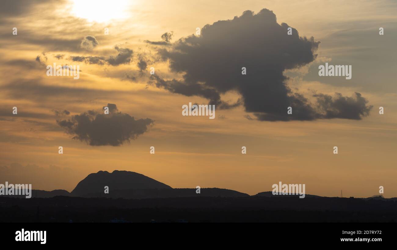 Silhouette d'une colline contre la belle lumière de l'heure d'or et de beaux nuages se forment à l'horizon avec le coucher du soleil Banque D'Images