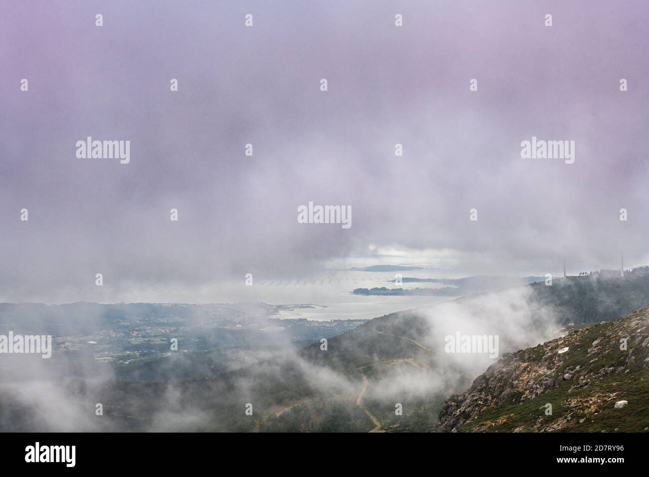 Vue aérienne de l'estuaire de la Ria de Arousa depuis la montagne de Muralla pendant un après-midi d'été brumeux, avec quelques éoliennes parmi les nuages. Banque D'Images