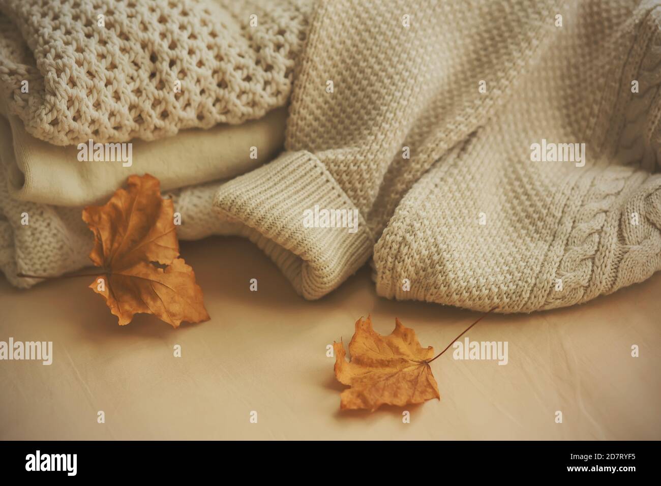 Sur un fond beige sont blancs woolen chaud pull pulls, et à côté d'eux deux feuilles d'érable sec. Vêtements chauds pour les journées froides d'automne. Octobre. Banque D'Images