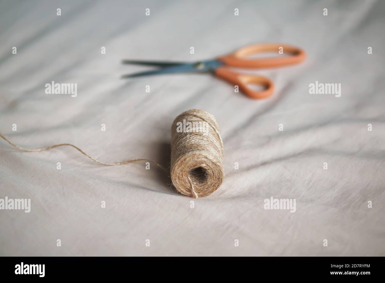 Sur le tissu doux et léger se trouve une bobine de corde de chanvre grossier et des ciseaux modernes pointus. Couture et passe-temps. Banque D'Images