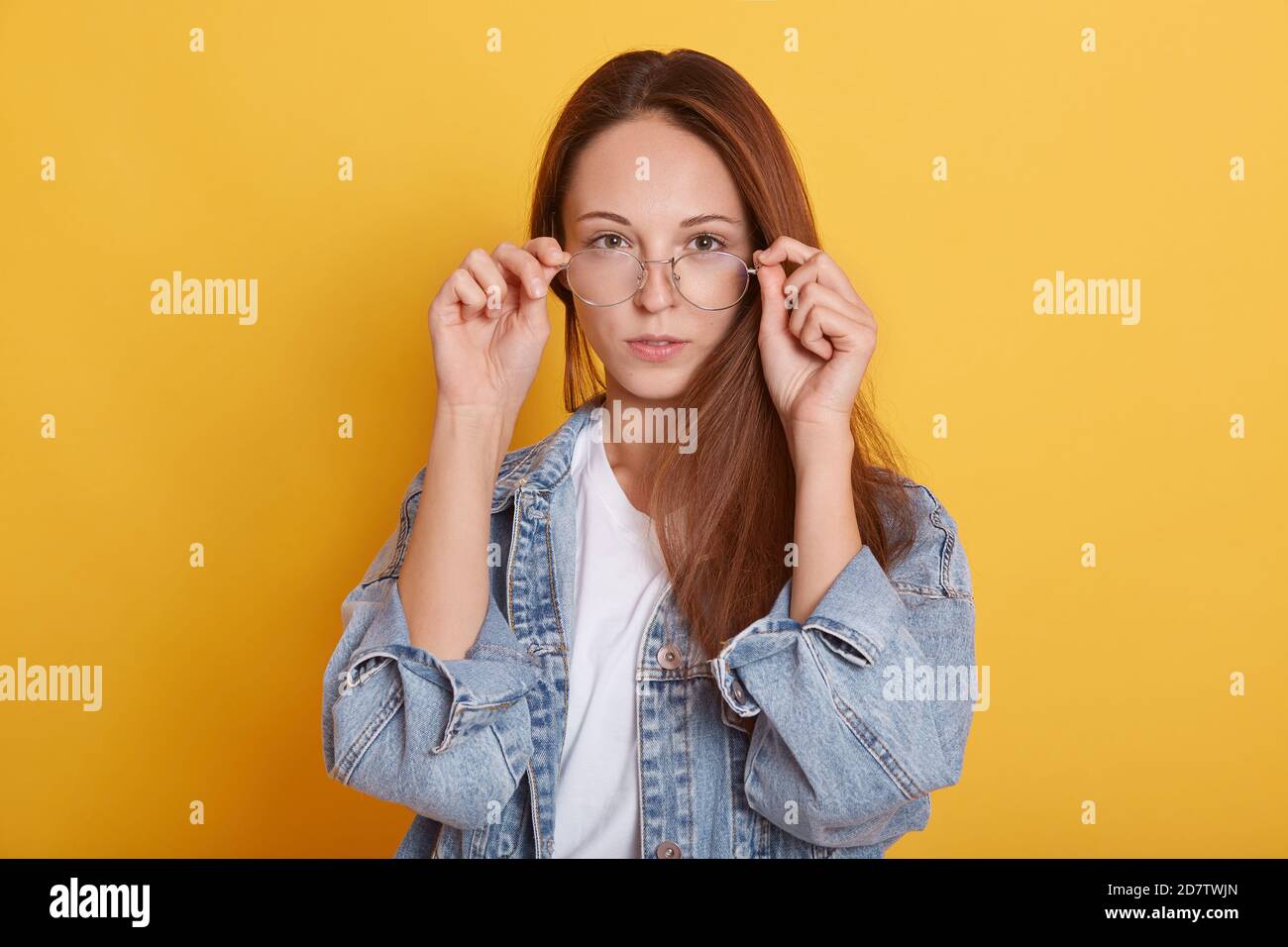 Image d'une adorable femme charismatique à cheveux longs, portant un t-shirt blanc décontracté et une veste en denim, qui regarde directement Banque D'Images