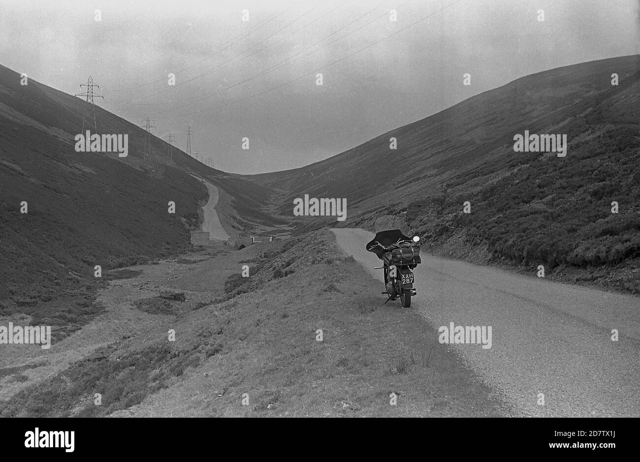 Années 1950, historique, une moto avec Faring garée sur une route étroite vide à voie unique dans une vallée dans les Highlands, en Écosse, au Royaume-Uni. Banque D'Images