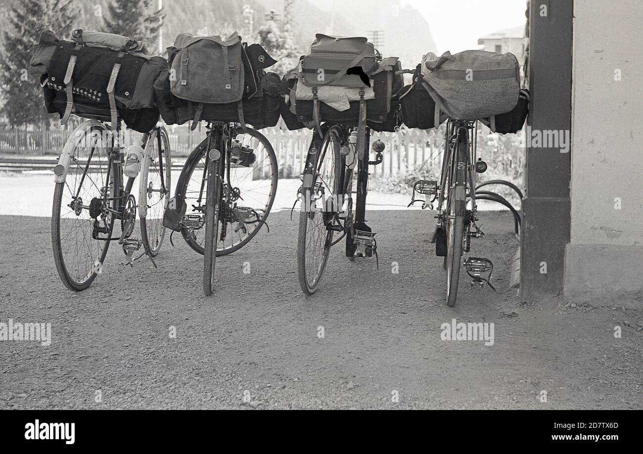 1950s, historique, quatre vélos de tourisme de l'époque se trouvaient sur le gravier par un poteau, vu de l'arrière, avec des pinces de pédale en métal et des sacs de toile traditionnels attachés. Banque D'Images