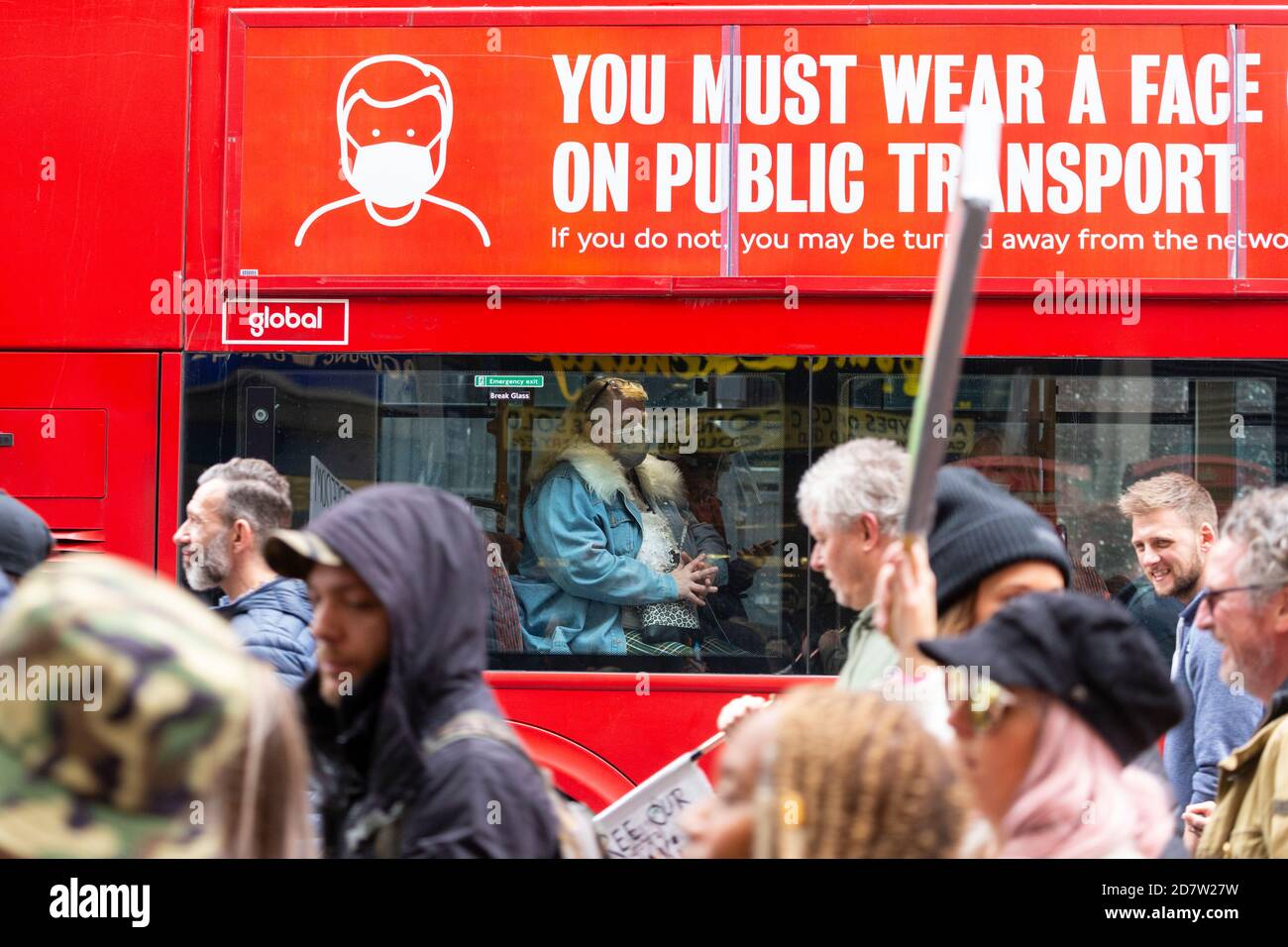 Les manifestants défilent devant une femme portant un masque sur un bus portant une signalisation COVID-19 lors d'un rassemblement anti-verrouillage à Londres, le 24 octobre 2020 Banque D'Images