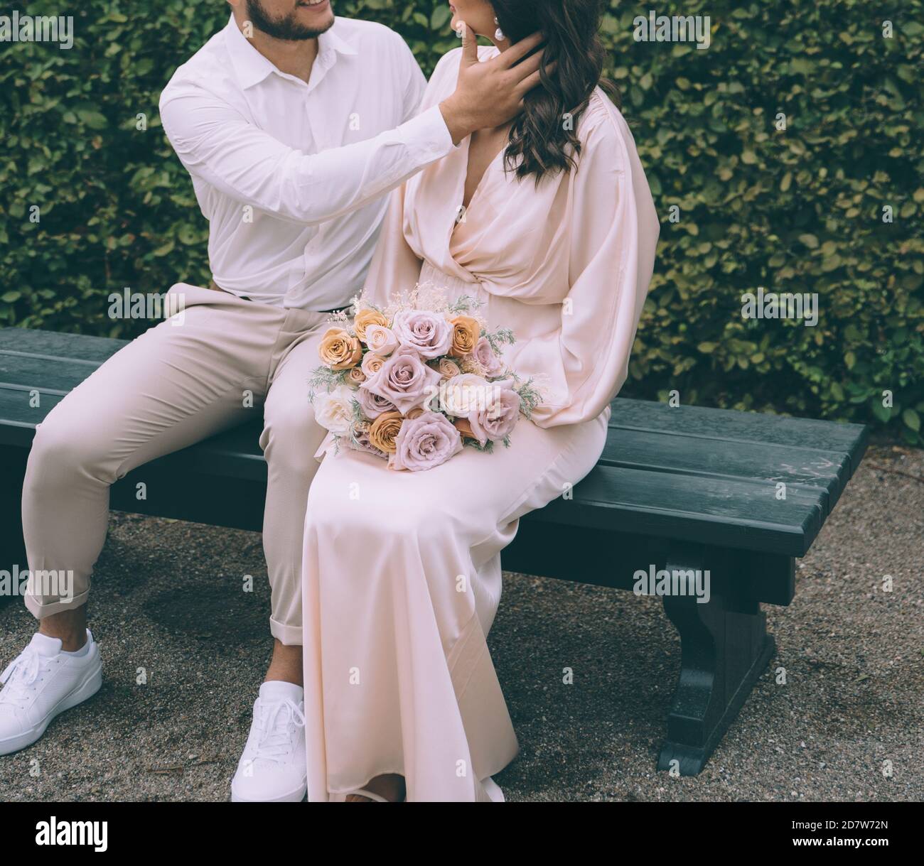 Couple de mariée embrassant sur un banc. Belle mariée avec un bouqet. Concept de photographie de mariage. Banque D'Images Couple de mariée embrassant sur un banc. Belle mariée avec un bouqet. Concept de photographie de mariage. Banque D'Images
