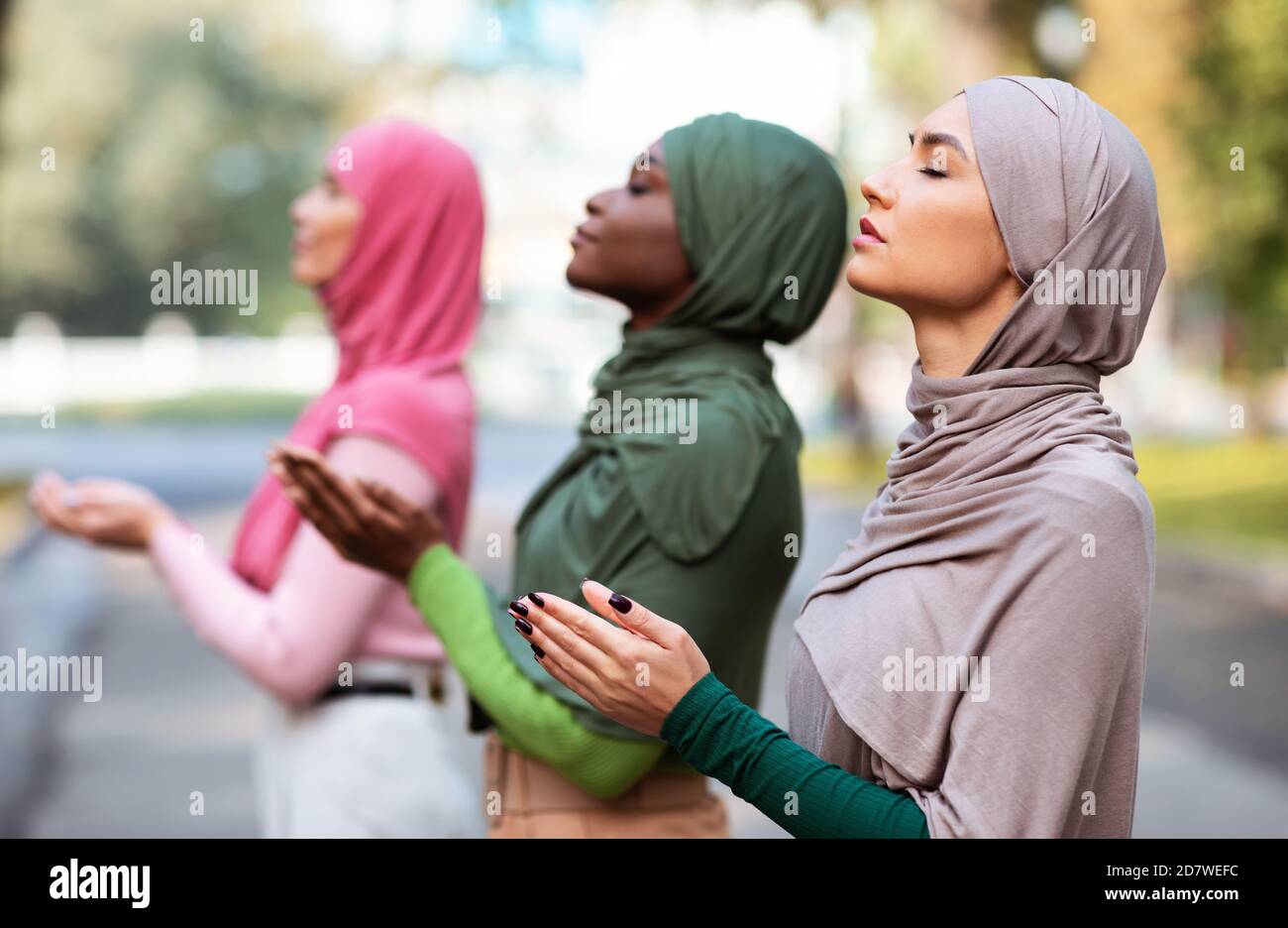 Trois musulmanes priant ensemble debout à l'extérieur en portant le hijab traditionnel Banque D'Images