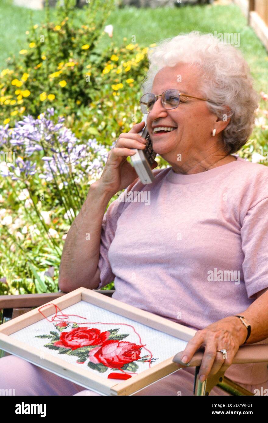 Une femme senior parle d'un téléphone portable à bouton-poussoir obsolète sur son patio, 190s, États-Unis Banque D'Images