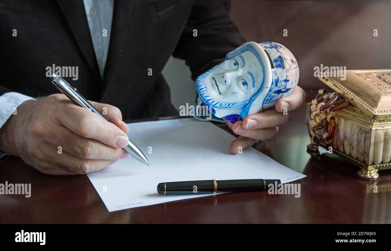 Les mains d'un homme: D'une main il tient son stylo, de l'autre main une banque de porcelaine Delft, nous voyons aussi une boîte à bijoux, évaluation, fiduciaire autorisé. Banque D'Images