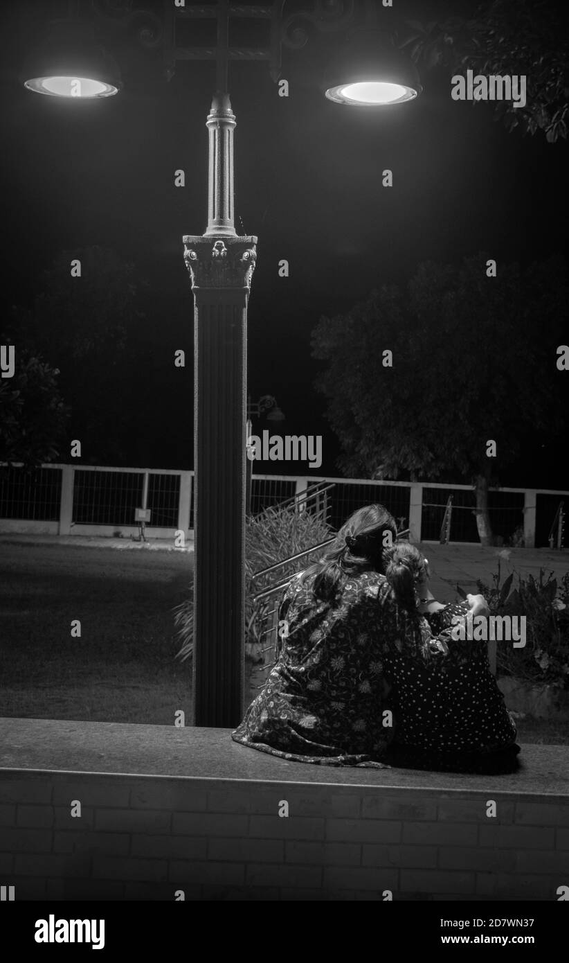 Mère et fille assises près d'un lampadaire et ayant un conversation Banque D'Images