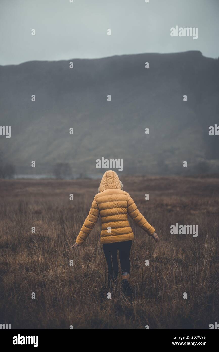 Femme marchant portant une veste en duvet jaune, appréciant le mode de vie de voyage de paysage Banque D'Images