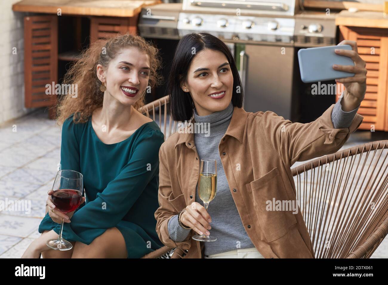 Portrait de deux femmes élégantes prenant des photos de selfie et souriant à l'appareil photo tout en profitant de la fête en plein air sur la terrasse, espace de copie Banque D'Images