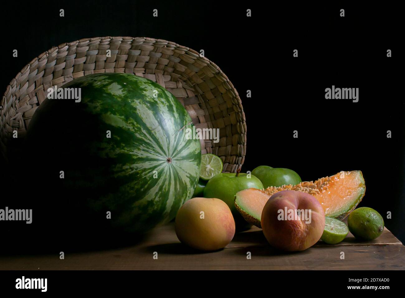 photographie de nourriture sombre, fruits sur une table en bois avec un panier fait à la main sur le fond, avec pastèque, pêches, citrons de melon et pommes vertes Banque D'Images