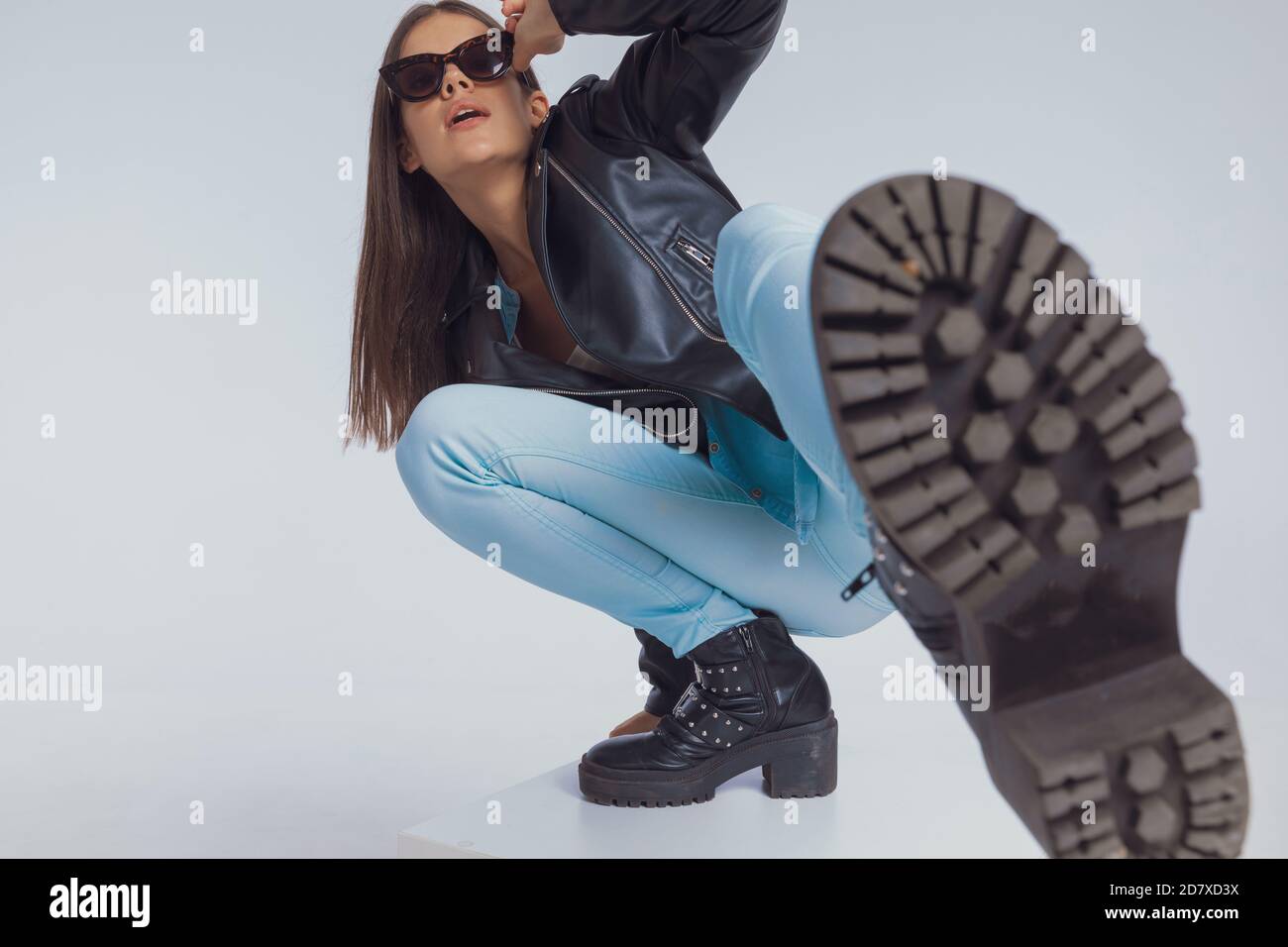 Charmant modèle de mode ajuster des lunettes de soleil et de frapper avec  sa jambe, crouching sur fond gris studio Photo Stock - Alamy