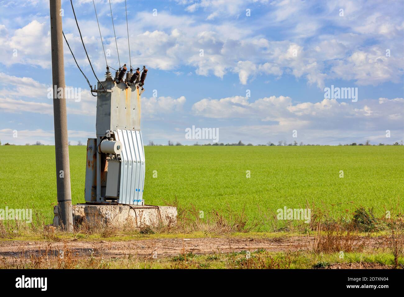 Une ancienne station de transformation se trouve au milieu d'un champ vert, près d'un pilier en béton, contre un ciel bleu nuageux. Banque D'Images