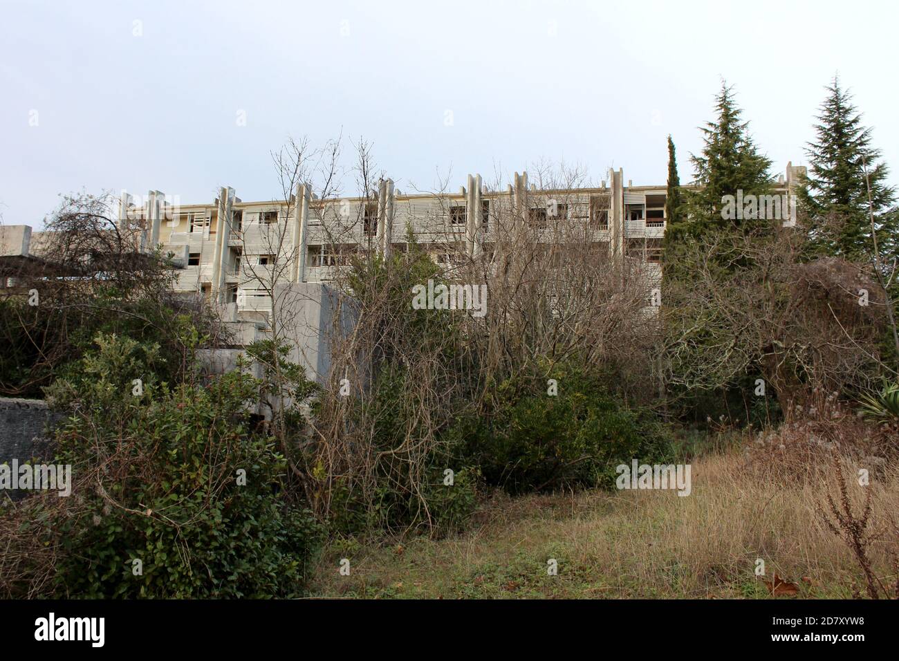 Abandonnés créepy regardant de grands vieux arbres sans feuilles mélangées avec Pins vert foncé devant l'époque de la Guerre froide hôtel en ruine Banque D'Images