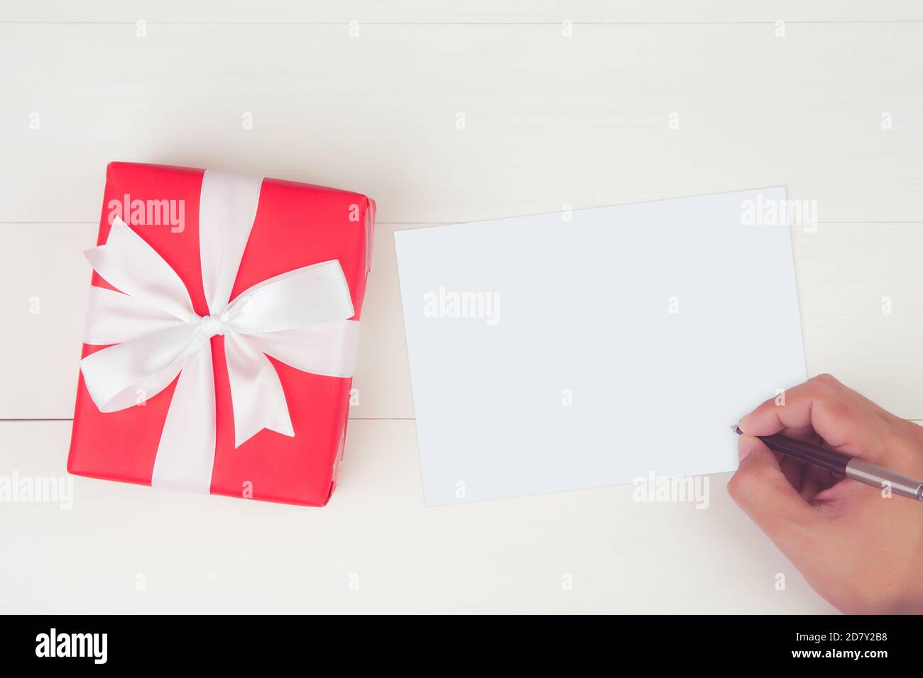 Main de l'homme écrire une lettre avec carte de voeux vierge et avoir une  boîte cadeau rouge sur table en bois, cadeau et paquet, maquette de carte  postale, vue du dessus, plat
