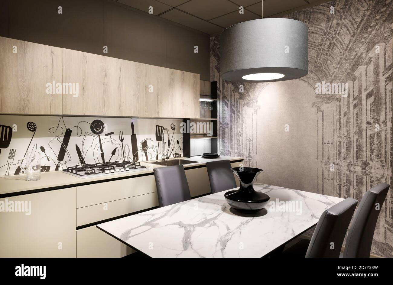 Cuisine moderne équipée avec dosseret décoratif et mur avec une table à manger et des chaises sous un plafonnier suspendu éclairant la pièce Banque D'Images