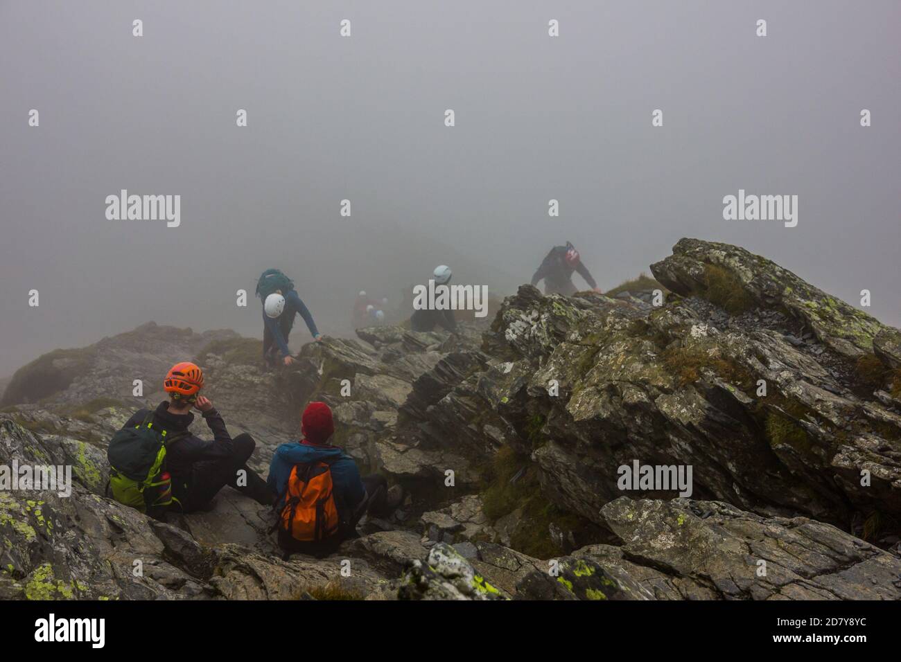 Groupe de mountaineers portant un casque prendre un repos dans la brume sur les rochers sur le sommet de la montagne après s'être brouté dans le Lake District en Angleterre. Banque D'Images