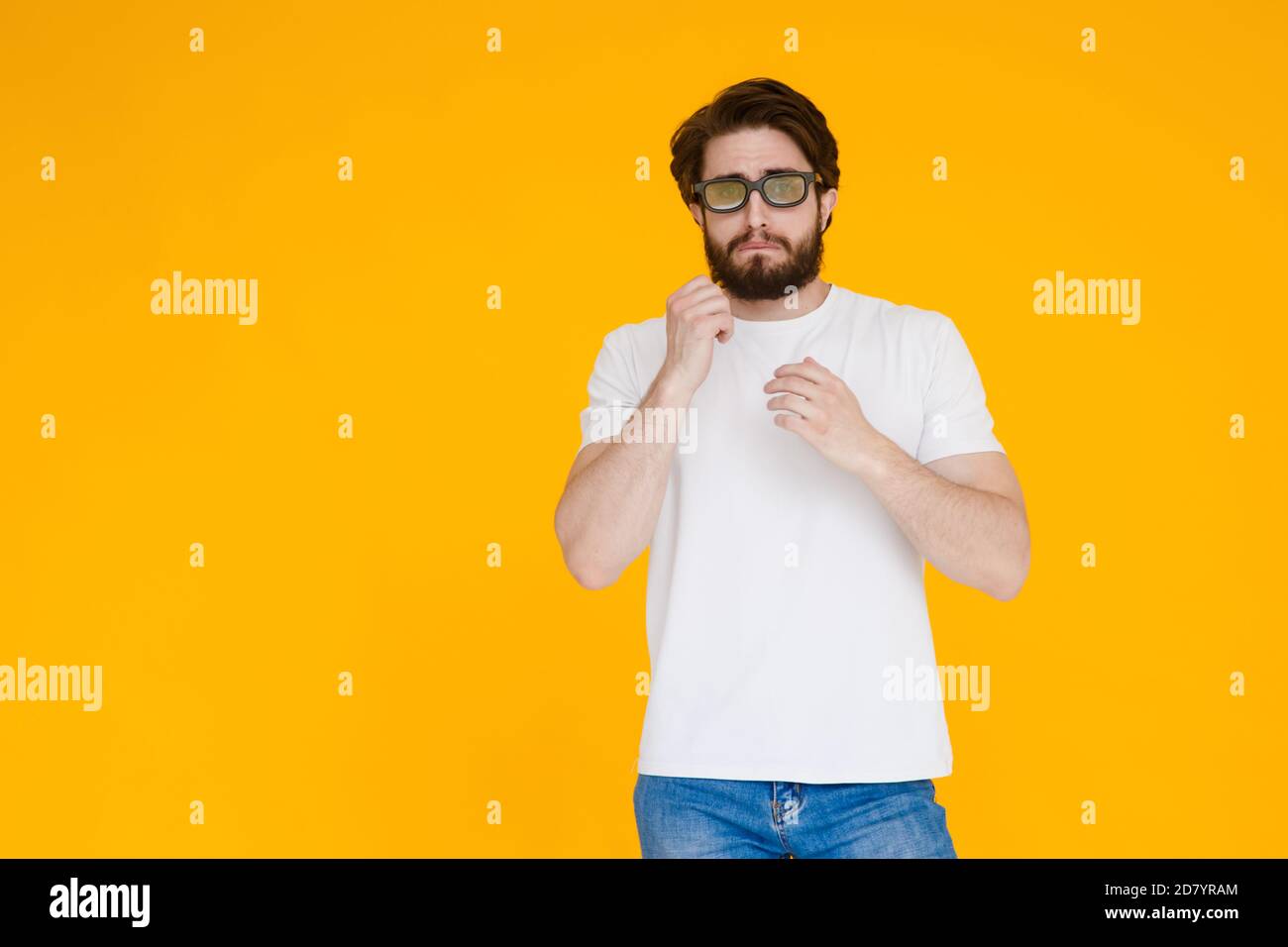 Jeune homme barbu dans un t-shirt blanc avec 3D les lunettes regardent un film mélodrame sur fond jaune Banque D'Images