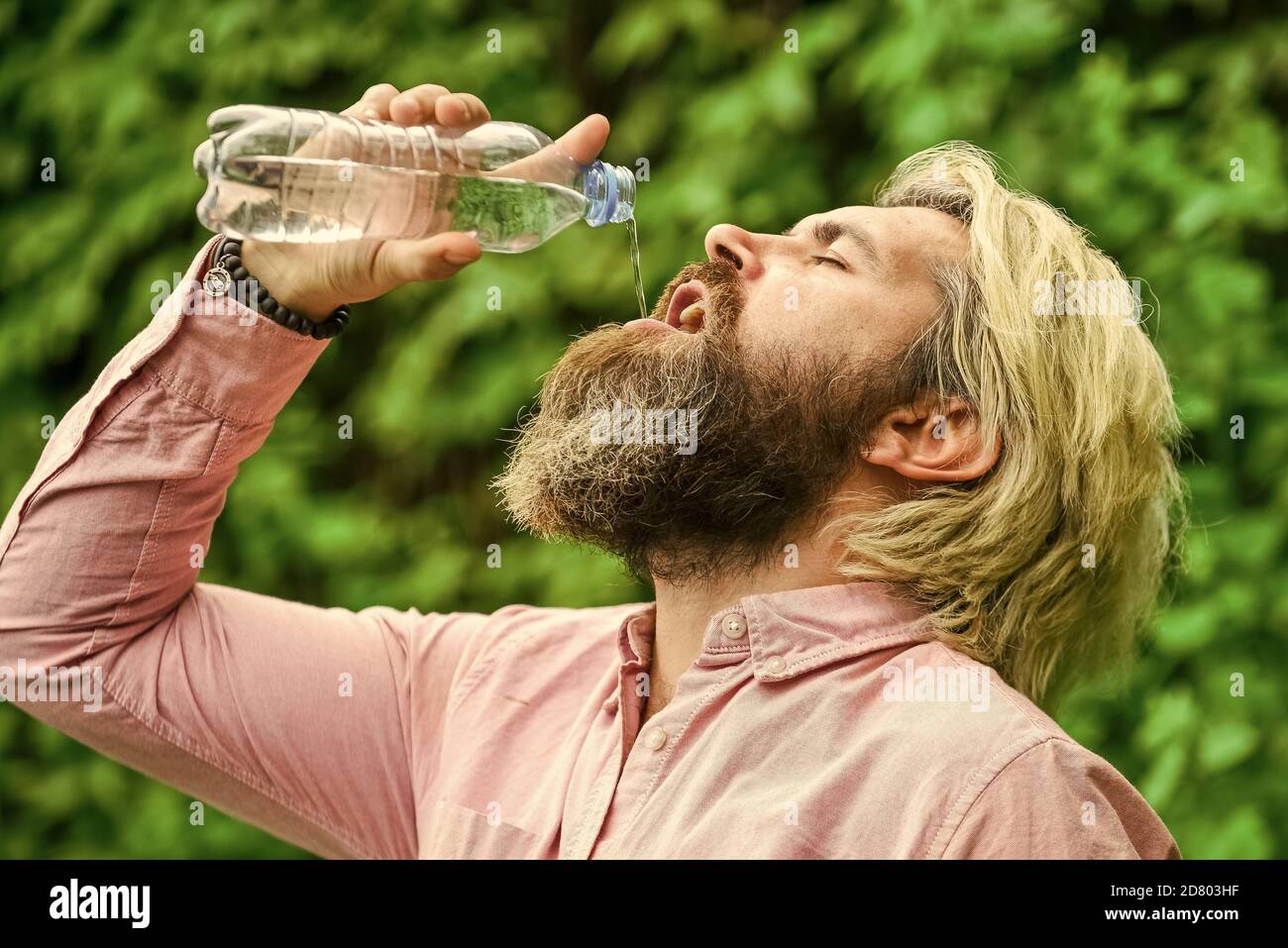 Équilibre de l'eau. Homme barbu touriste eau potable bouteille plastique nature fond. Chaleur estivale. Boire de l'eau claire. Un gars assoiffé qui boit de l'eau en bouteille Un mode de vie sain. Sécurité et santé. Banque D'Images