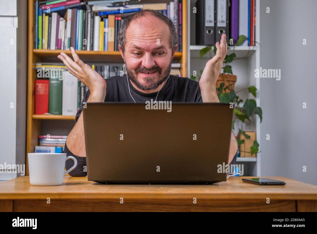 Homme travaillant en ligne depuis la maison sur un ordinateur portable derrière un bureau d'époque, avec des écouteurs, parlant et expliquant à des collègues lors d'une réunion en ligne Banque D'Images