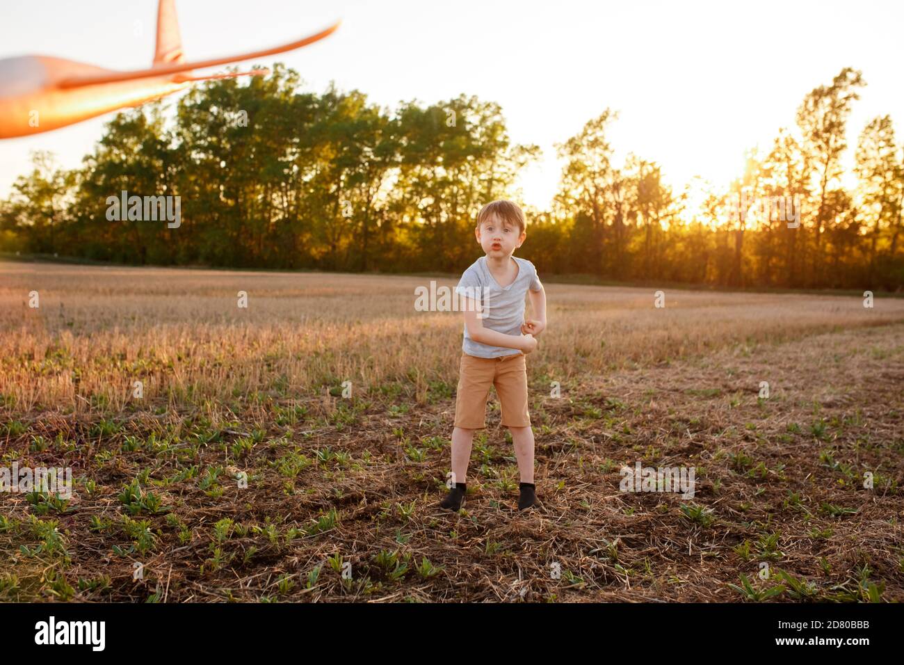 Un enfant heureux court avec un avion jouet sur un fond de coucher de soleil sur un champ. Le concept d'une famille heureuse. Rêves d'enfance Banque D'Images