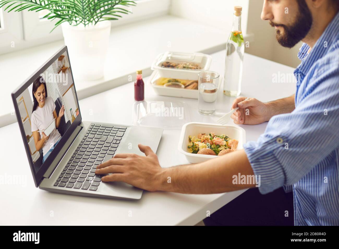 Jeune homme ayant un déjeuner virtuel avec sa femme ou sa petite amie pendant pause au travail ou au bureau à domicile Banque D'Images