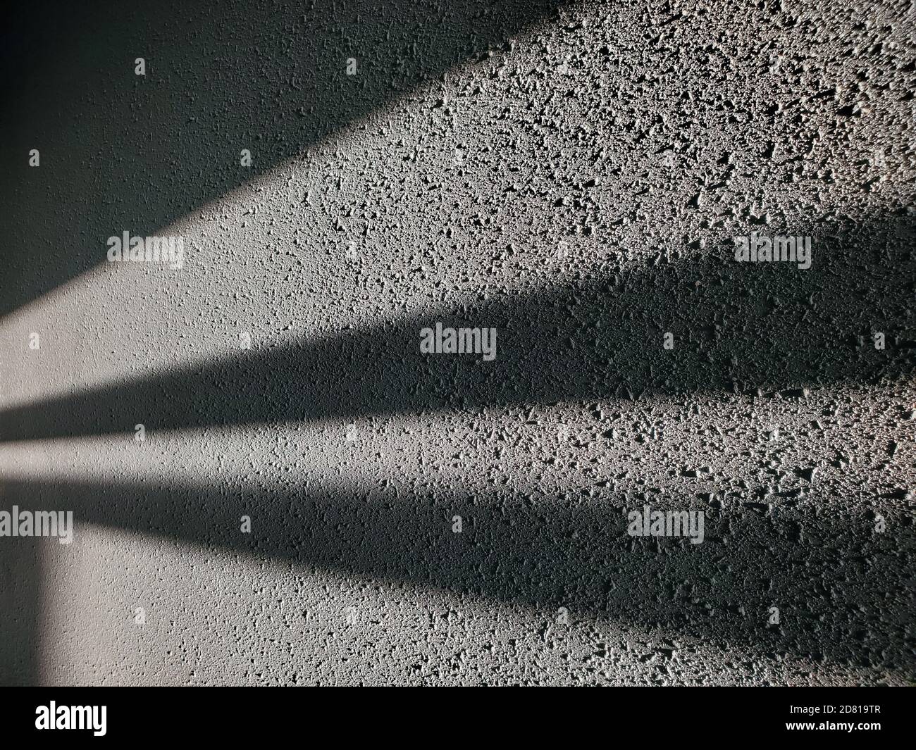 Les ombres géométriques abstraites ressemblent à des rayons de lumière dans l'obscurité. Mur en plâtre rugueux avec surface colorée grise et rayures de lumière et d'ombre Banque D'Images