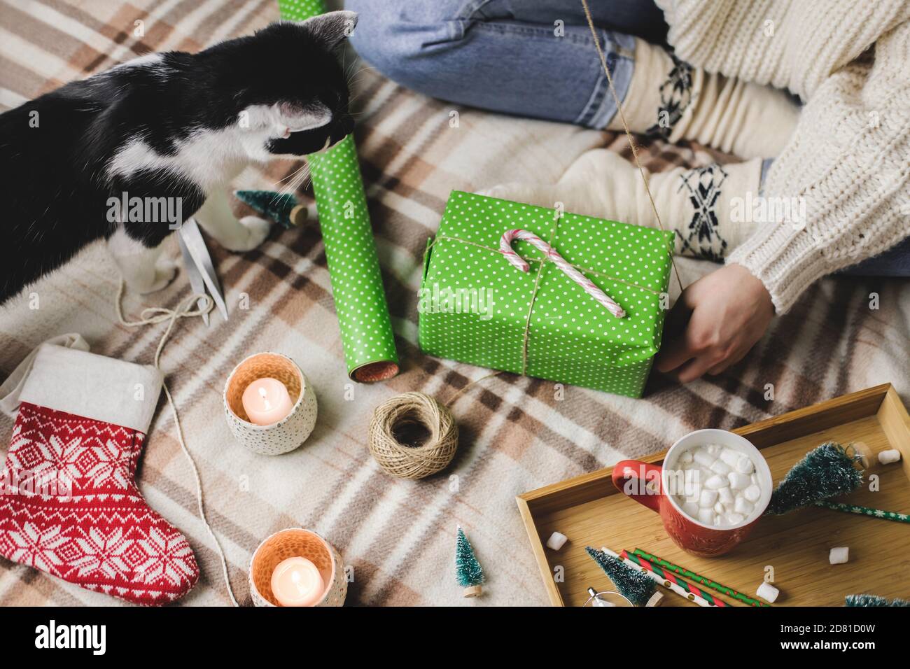 Une jeune femme est assise sur un tissu écossais dans un confortable pull blanc en laine, des chaussettes et des enveloppements cadeau de Noël en papier d'emballage à pois. Tuxe noir et blanc amusant Banque D'Images