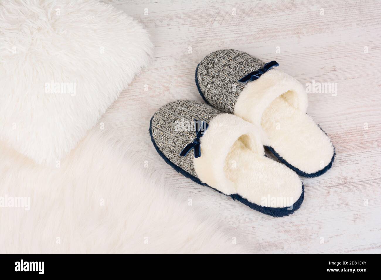 Paire de chaussons féminins chauds sur un tapis de fourrure blanc. Banque D'Images