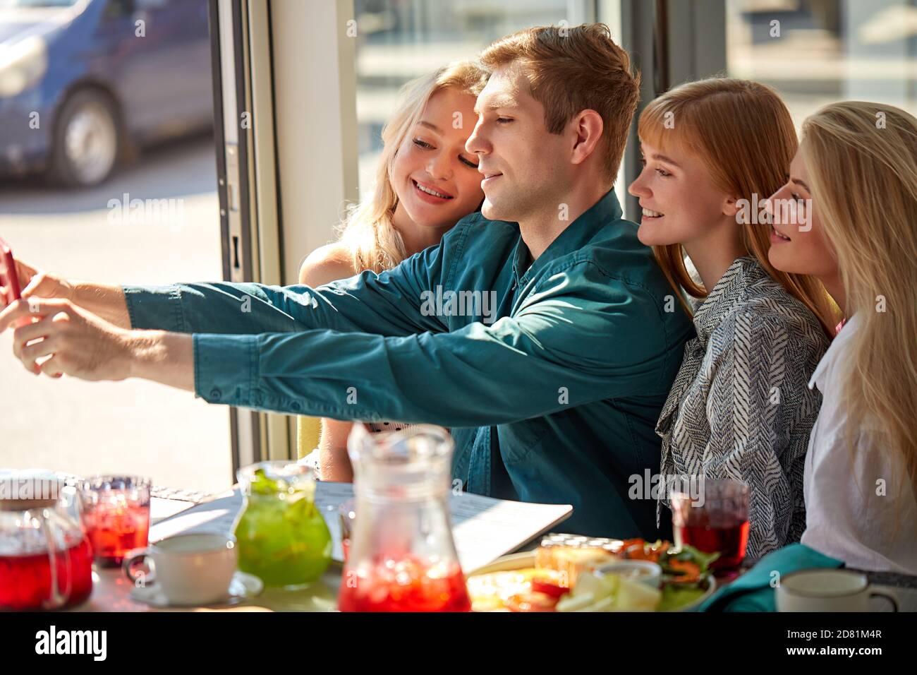 les caucasiens débordant de joie posant pour la photo dans un café ensemble, emportant le selfie sur un smartphone, posant pour la photo dans un café ensemble, enregistrant la vidéo pour le réseau social, s'amusant avec des amis. vue latérale Banque D'Images