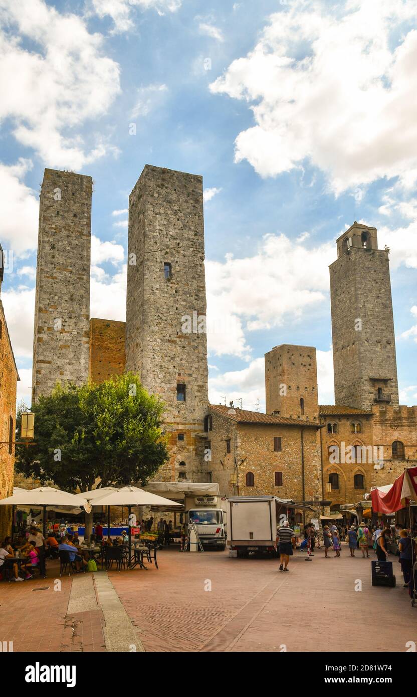 Vue sur la Piazza delle Erbe avec les gens au café en plein air et au marché local sous les célèbres tours médiévales, San Gimignano, Sienne, Toscane, Italie Banque D'Images