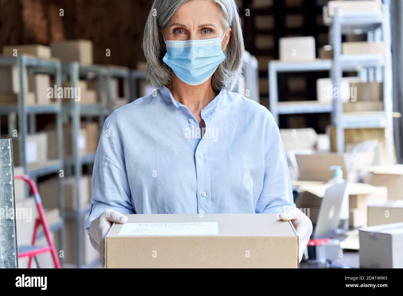 Femme entrepreneur plus âgée portant un masque facial tenant une boîte à colis, portrait. Banque D'Images