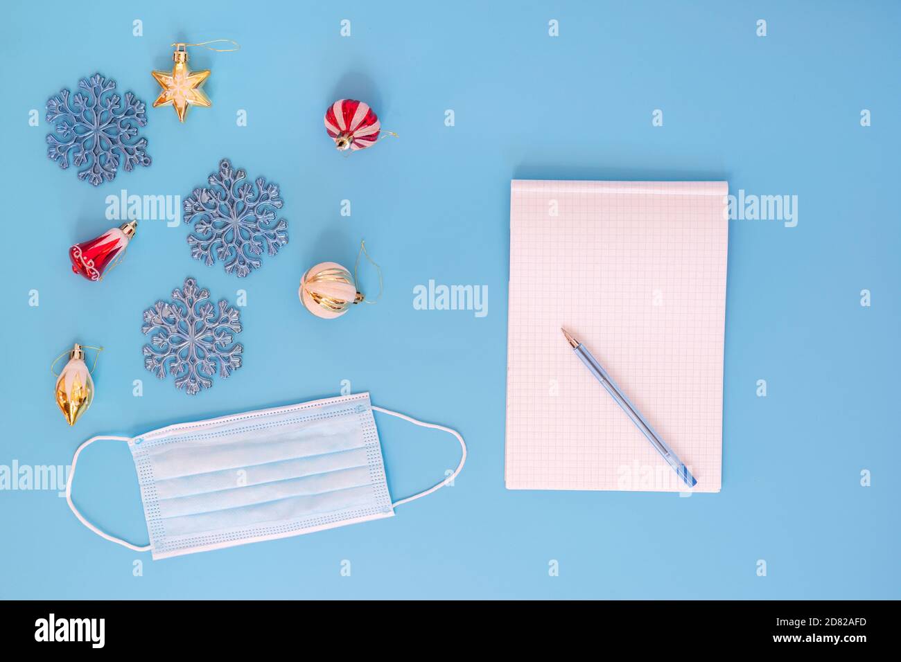 Jouets de Noël et masque médical sur fond bleu. Un Bloc-notes propre pour la rédaction des plans pour l'année à venir et un stylo. Concept de vacances pendant Banque D'Images