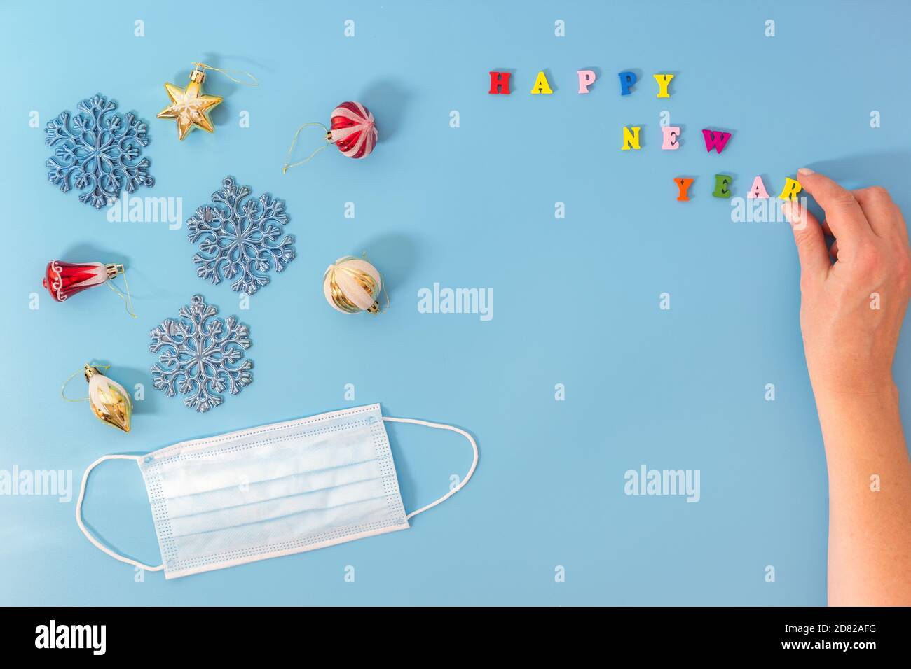 Jouets de Noël et masque médical sur fond bleu. Main présente l'inscription Bonne Année. Le concept d'un congé pendant la période du Banque D'Images