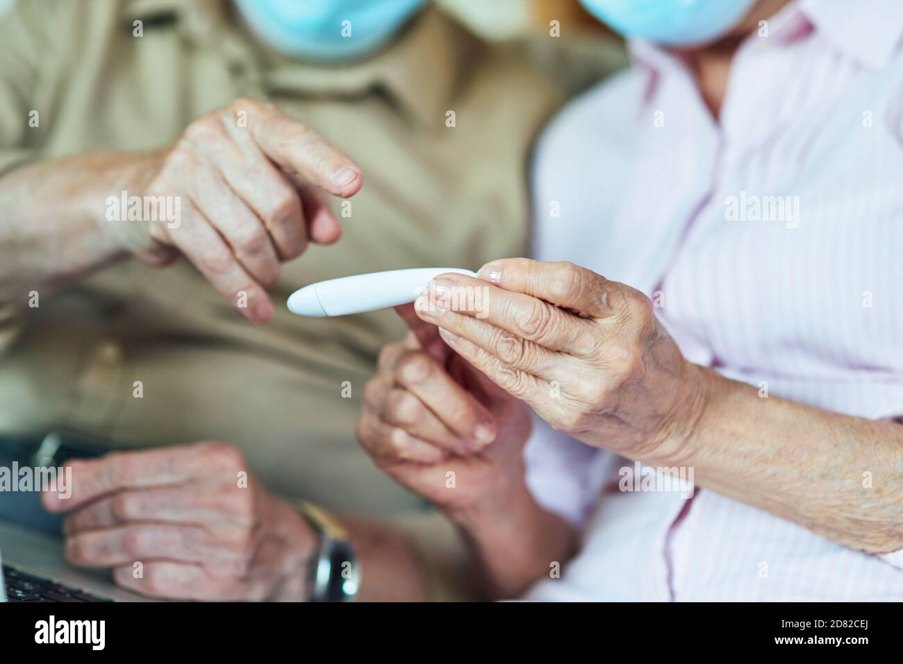 Photo rognée d'une femme âgée dans un masque de protection vérifiant la température pendant que son mari est assis à côté d'elle. Concept de soins et de santé Banque D'Images