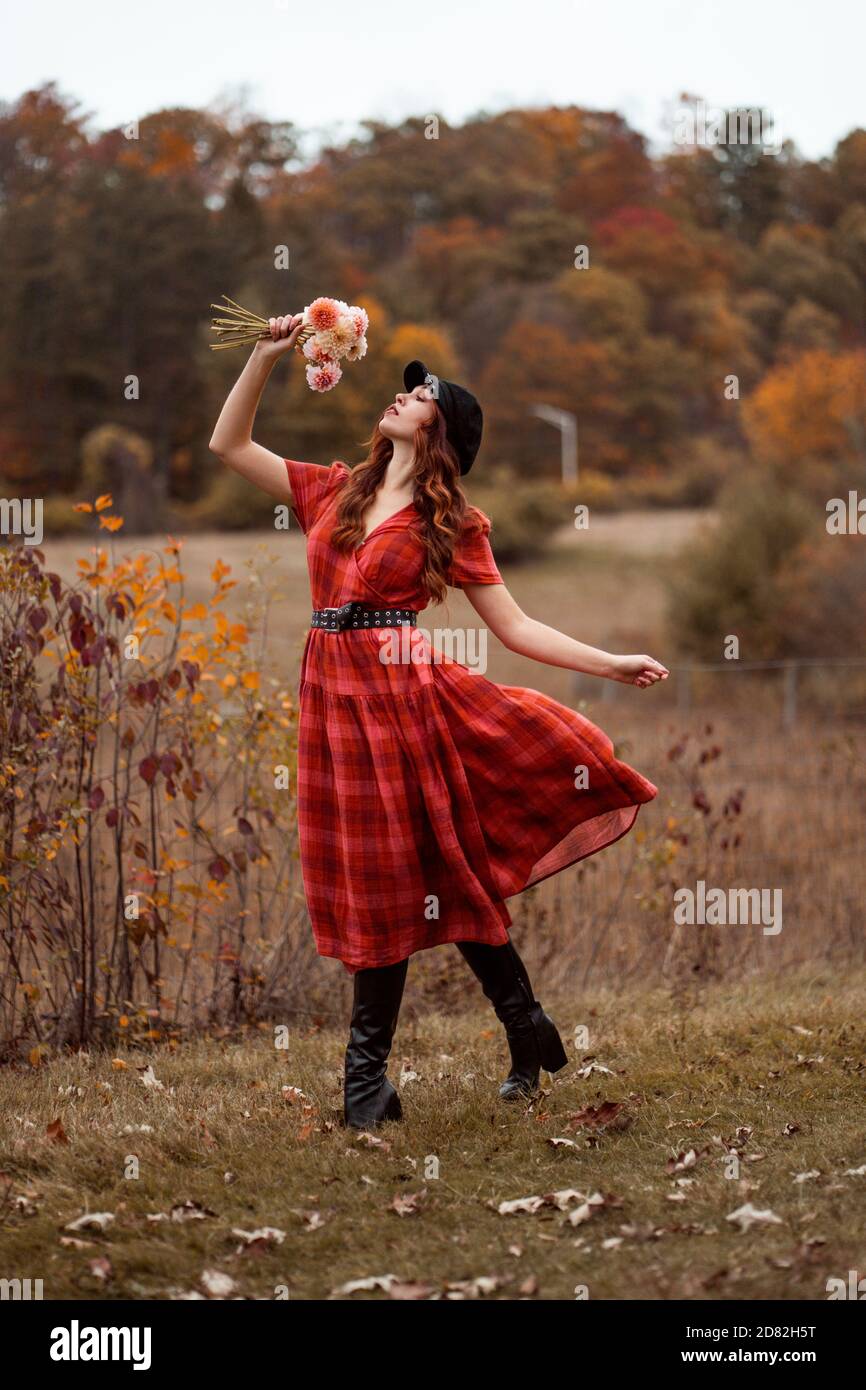 Jeune femme en robe de mode Plaid posant avec bouquet de fleurs En automne  de paysage de feuillage Photo Stock - Alamy