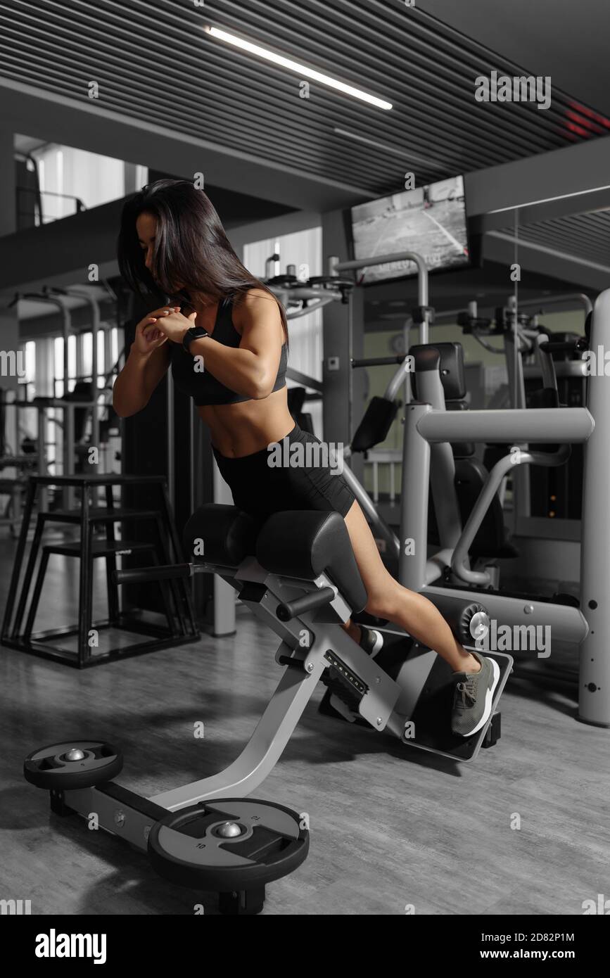 Jeune femme sportive fille tout en effectuant l'exercice d'hyperextension en utilisant la machine d'équipement pour l'entraînement de dos. Vue latérale de l'entraînement sexy de fille athlétique. Concept de soins de santé et de conditionnement physique Banque D'Images