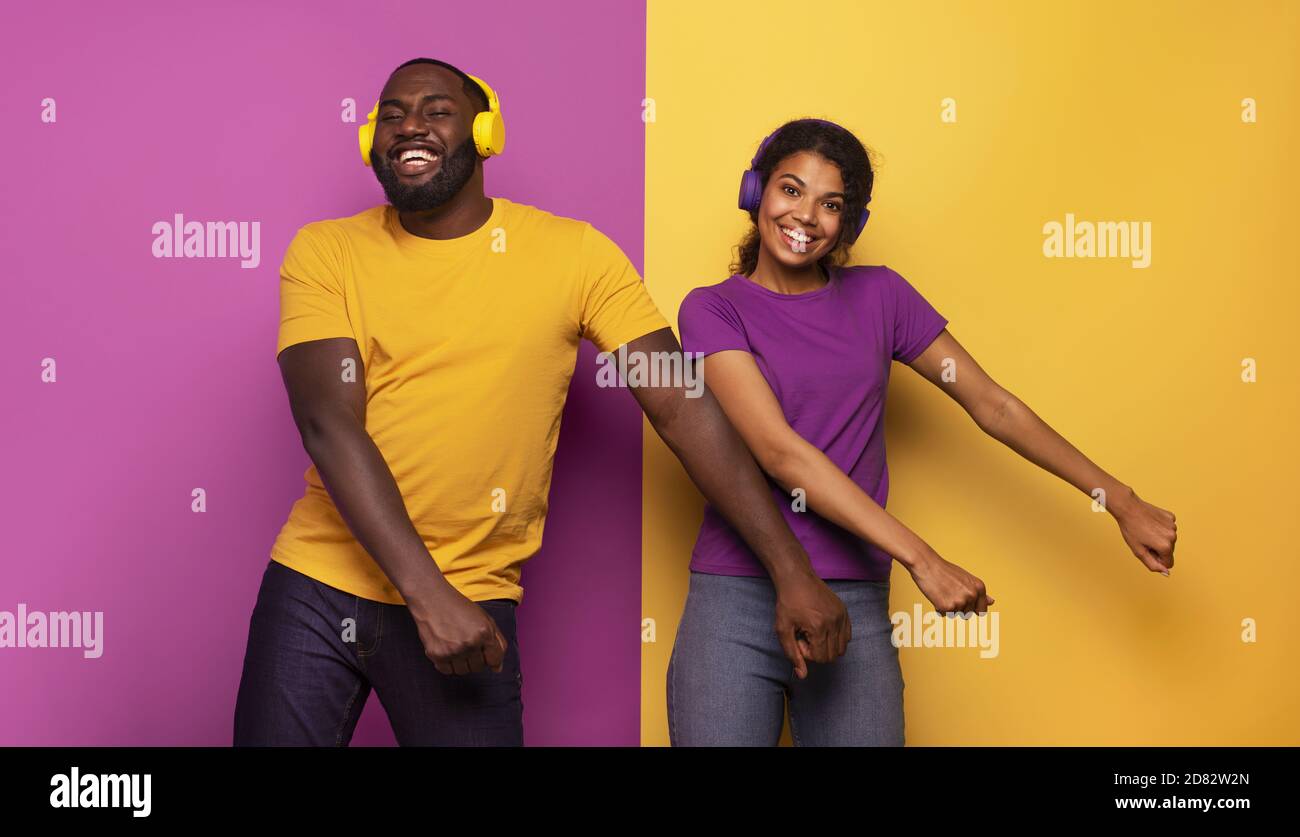 Couple avec casque écouter de la musique et danser avec énergie sur fond violet et jaune Banque D'Images