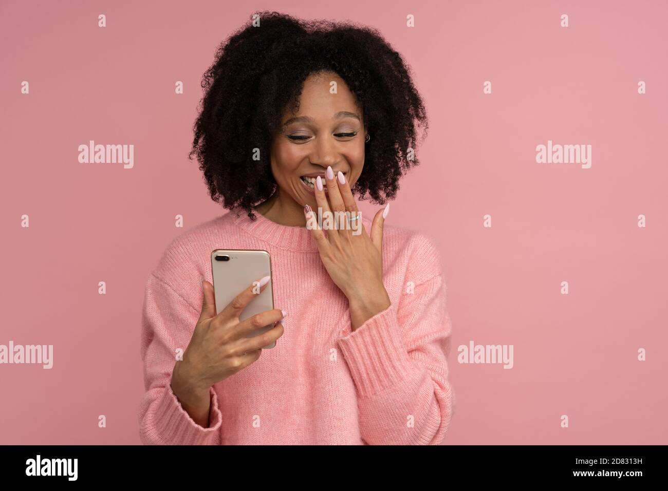 Femme millénaire souriante à la peau sombre, regardant un téléphone mobile en état de choc, couvrant sa bouche large avec la main, lisant le message de son ami, confit Banque D'Images