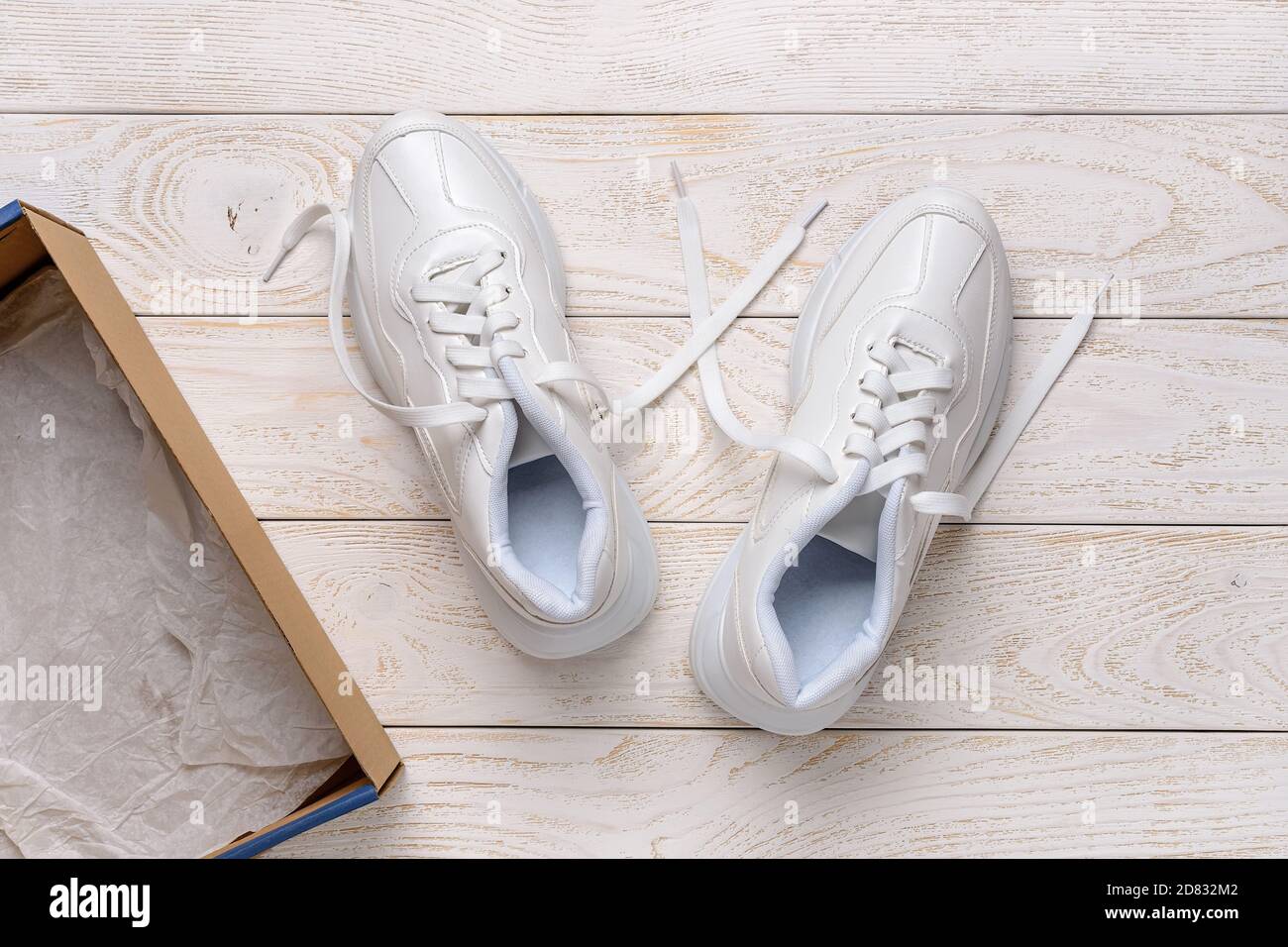 Paire de sneakers à grosse semelle blanche près d'une boîte en carton  marron sur un sol en bois blanc. Boîte ouverte avec de nouvelles chaussures  confortables pour un style de vie actif