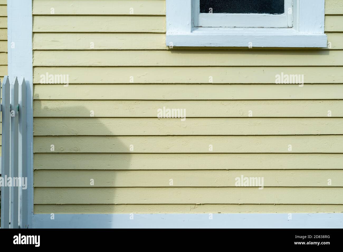 Le mur extérieur d'une maison en bois tapissé jaune avec bordure blanche autour d'une fenêtre en verre fermée. Banque D'Images