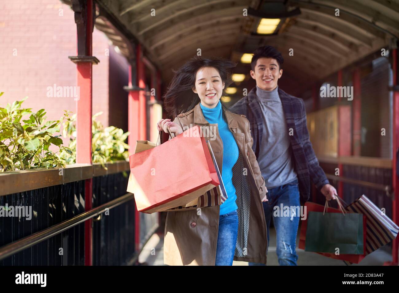 un jeune couple asiatique court sur un passage pour piétons avec des sacs de shopping entre les mains heureux et souriant Banque D'Images