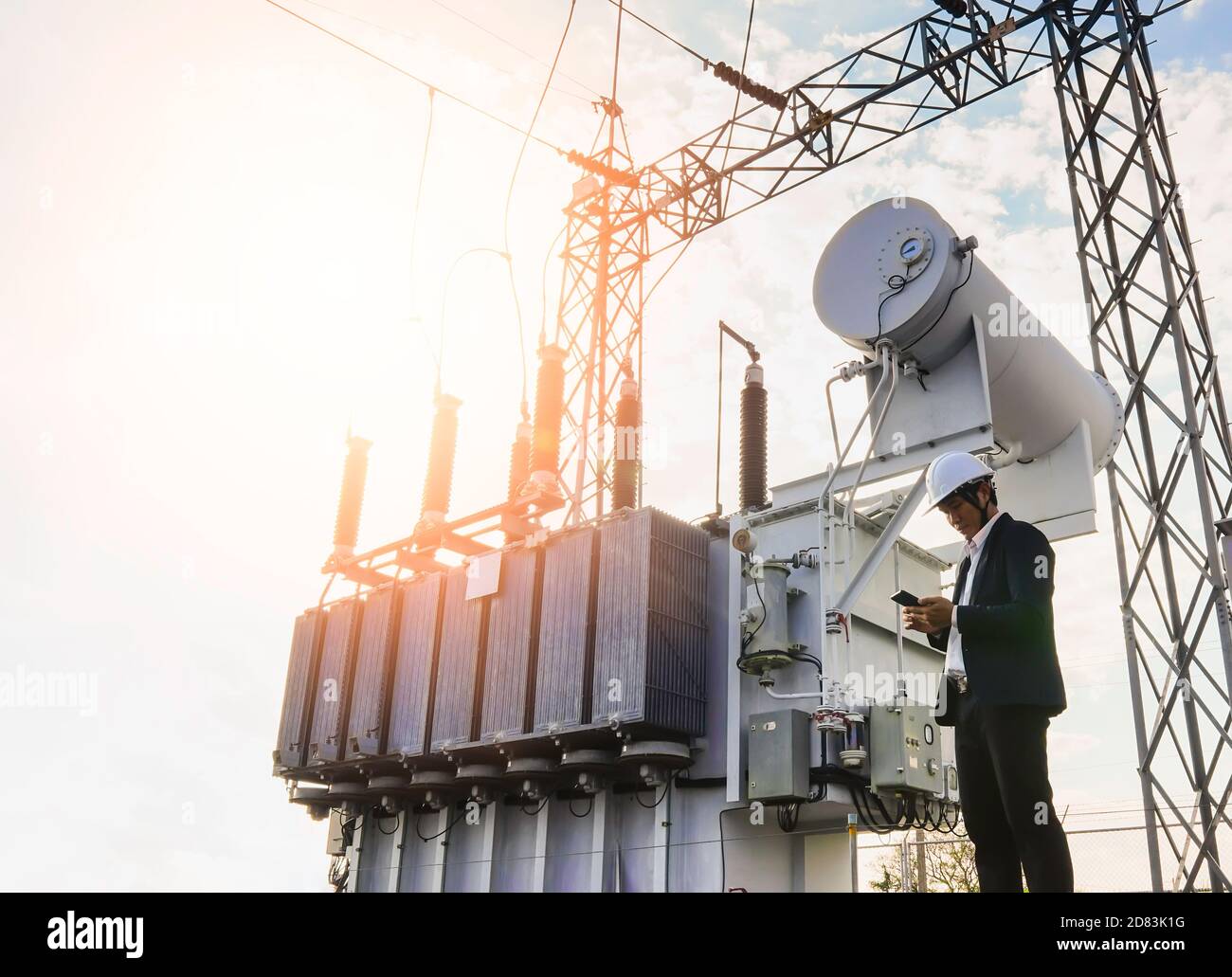 Image d'un homme d'affaires portant un costume noir, debout regardant un grand transformateur de puissance avec ciel bleu comme arrière-plan, concept à propos de b Banque D'Images